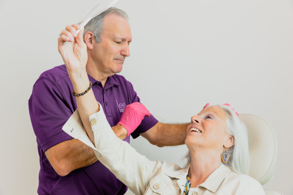 A patient holds a handheld mirror during a consultation to learn more about a brow lift near Jupiter Island.