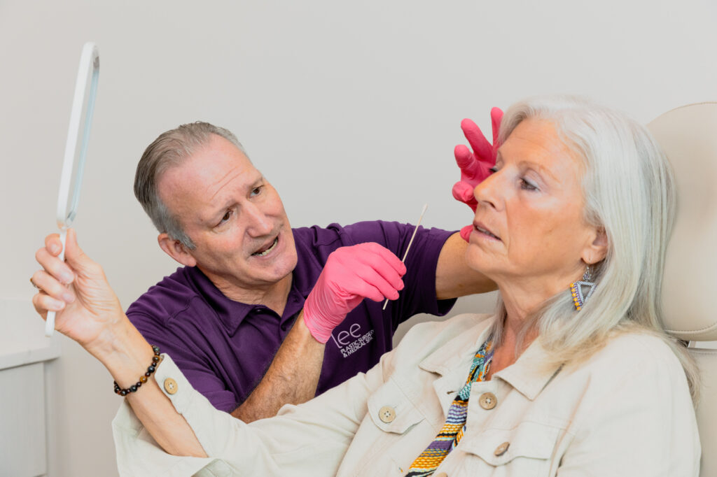 A patient looks in a handheld mirror as she meets with Dr. Lee to discuss undergoing a facelift near Jupiter Island.